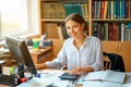 Young happy business lady in white shirt sitting at table with computer and papers working environment Royalty Free Stock Photo