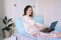 Young happy business woman lies in bed in pajamas in a cozy home. Online working, studying from home with laptop. Freelancer Royalty Free Stock Photo