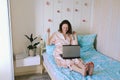 Young happy business woman lies in bed in pajamas in a cozy home. Online working, studying from home with laptop. Freelancer Royalty Free Stock Photo