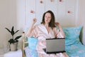 Young happy business woman lies in bed in pajamas in a cozy home. Online working, studying from home with laptop. Freelancer Royalty Free Stock Photo