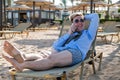 Young happy businessman downshifter talks on the phone lying on a sun lounger in the middle of the beach in a shirt, tie