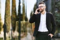 Young happy businessman in glasses walking outside on sunny day and speaking on mobile phone with close friend or family Royalty Free Stock Photo