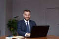 Young happy businessman smiling while using his laptop. Portrait of smiling business man reading message and working in office. Royalty Free Stock Photo