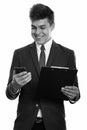 Young happy businessman smiling while using mobile phone and holding clipboard Royalty Free Stock Photo