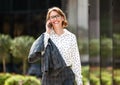 Young happy businesswoman in formal outfit walking outside on sunny day and speaking on mobile phone Royalty Free Stock Photo