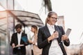 Happy businesswoman holding digital tablet and coffee to go outside of modern building, businesspeople in background Royalty Free Stock Photo