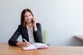 Young happy businesswoman talking on the phone and writing notes in office Royalty Free Stock Photo