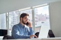 Young happy busy latin business man talking on phone using laptop in office. Royalty Free Stock Photo