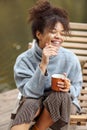 Young happy carefree african american woman with cup of hot tea relaxing near pond in autumn nature Royalty Free Stock Photo