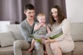 Young happy caring parents reading a book to their child while sitting on the sofa at home.Family holidays,education Royalty Free Stock Photo