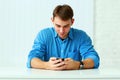 Young happy casual businessman sitting at the table and typing on smartphone Royalty Free Stock Photo