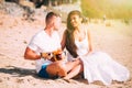 Young happy Caucasian adult romantic couple play ukulele guitar in casual lifestyle on summer beach.