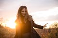 Young happy caucasian brunette woman walking through grassy meadow at sunset and smiling Royalty Free Stock Photo