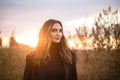 Young happy caucasian brunette woman walking through grassy meadow at sunset and smiling Royalty Free Stock Photo