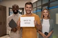 Young happy caucasian man, office worker showing paper with text BACK TO OFFICE at camera and smiling while standing Royalty Free Stock Photo