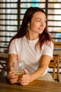 Young woman sits at wooden table with cup, on terrace of cafe with striped background and flowers in summer Royalty Free Stock Photo