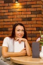 Young happy caucasian woman with brown hair sitting in cafe near a brick wall with book at the table Royalty Free Stock Photo