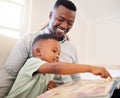 Young happy cheerful African american father reading a book with his son sitting on the couch at home. Little boy Royalty Free Stock Photo