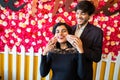 Young happy cheerful indian couple in love have fun together, man pinching cheeks of his girlfriend against floral background,