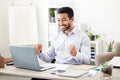 Young happy and cheerful mixed race businessman cheering with his fists while working on a laptop alone in an office at Royalty Free Stock Photo