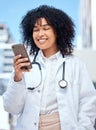 Young happy and cheerful mixed race female doctor with a curly afro using social media on a phone while on a break Royalty Free Stock Photo