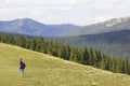 Young happy child boy with backpack walking in mountain grassy valley on background of summer woody mountain. Active lifestyle,