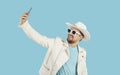 Young happy Caucasian man in sunglasses takes selfie on mobile phone, stands in turquoise studio Royalty Free Stock Photo