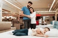 Young happy couple in background enjoying sleeping little girl. Choosing mattress in store. Royalty Free Stock Photo