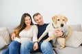 Young happy couple with dog sitting on sofa Royalty Free Stock Photo