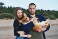 Young happy couple with dog standing on beach. Beautiful girl and guy and Corgi puppy having fun Royalty Free Stock Photo