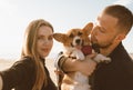 Young happy couple with dog take selfie on beach. Beautiful girl and guy and Corgi puppy Royalty Free Stock Photo