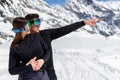 Young happy couple embrace, wear in goggles, man showing by arm a point a side. mountain landscape background. Royalty Free Stock Photo