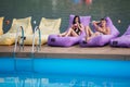 Young happy couple enjoying with drinks on cushioned loungers by swimming pool on the background of river