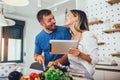 Happy couple is enjoying and preparing healthy meal in their kitchen and reading recipes on the digital tablet Royalty Free Stock Photo