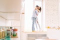 Young happy couple hugging on the windowsill in their apartment, sitting on the window in the sun