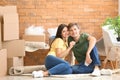 Young happy couple with key and moving boxes sitting on carpet at new home Royalty Free Stock Photo