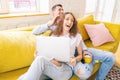 Young happy couple lies on a yellow sofa with a laptop in their apartment, online shopping and internet technology for home Royalty Free Stock Photo