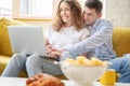 Young happy couple lies on a yellow sofa with a laptop in their apartment, online shopping and internet technology for home Royalty Free Stock Photo