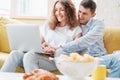 Young happy couple lies on a yellow sofa with a laptop in their apartment, online shopping and internet technology for home Royalty Free Stock Photo