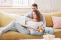 Young happy couple lies on a yellow sofa with a laptop in their apartment, online shopping and internet technology for home Royalty Free Stock Photo