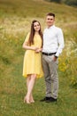 Young happy couple in love in a grass field in sunny day. girl in a yellow dress and a guy with a stylish haircut. portrait of Royalty Free Stock Photo