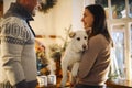 Young happy couple man and woman holding cute white dog and hugging while standing in kitchen decorated for Christmas Royalty Free Stock Photo