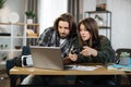 Young happy couple playing video games at home, sitting at the table with laptop and using joysticks Royalty Free Stock Photo