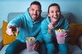 Young happy couple with popcorn sitting on sofa and watching funny comedy movie. Couple enjoying time together at home Royalty Free Stock Photo