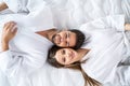 Young happy couple relaxing, lying in bed in white bathrobes, head to head, looking at camera and smiling Royalty Free Stock Photo