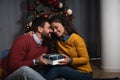 Young happy couple sitting at home in front of the Christmas tree decorated with decorations exchanging gifts for the New Year Royalty Free Stock Photo