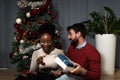 Young happy couple sitting at home in front of the Christmas tree decorated with decorations exchanging gifts for the New Year Royalty Free Stock Photo