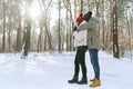 Young happy couple on sunny day in snow-covered park. Men and women are standing and hugging in a snowy winter park. Side view Royalty Free Stock Photo