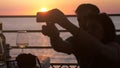 Silhouette of couple in love taking selfie photo with cellphone in beach cafe during beautiful sunset and drinking white Royalty Free Stock Photo