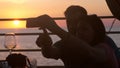 Young happy couple in love taking selfie photo with cellphone in beach cafe during beautiful sunset and drinking white Royalty Free Stock Photo